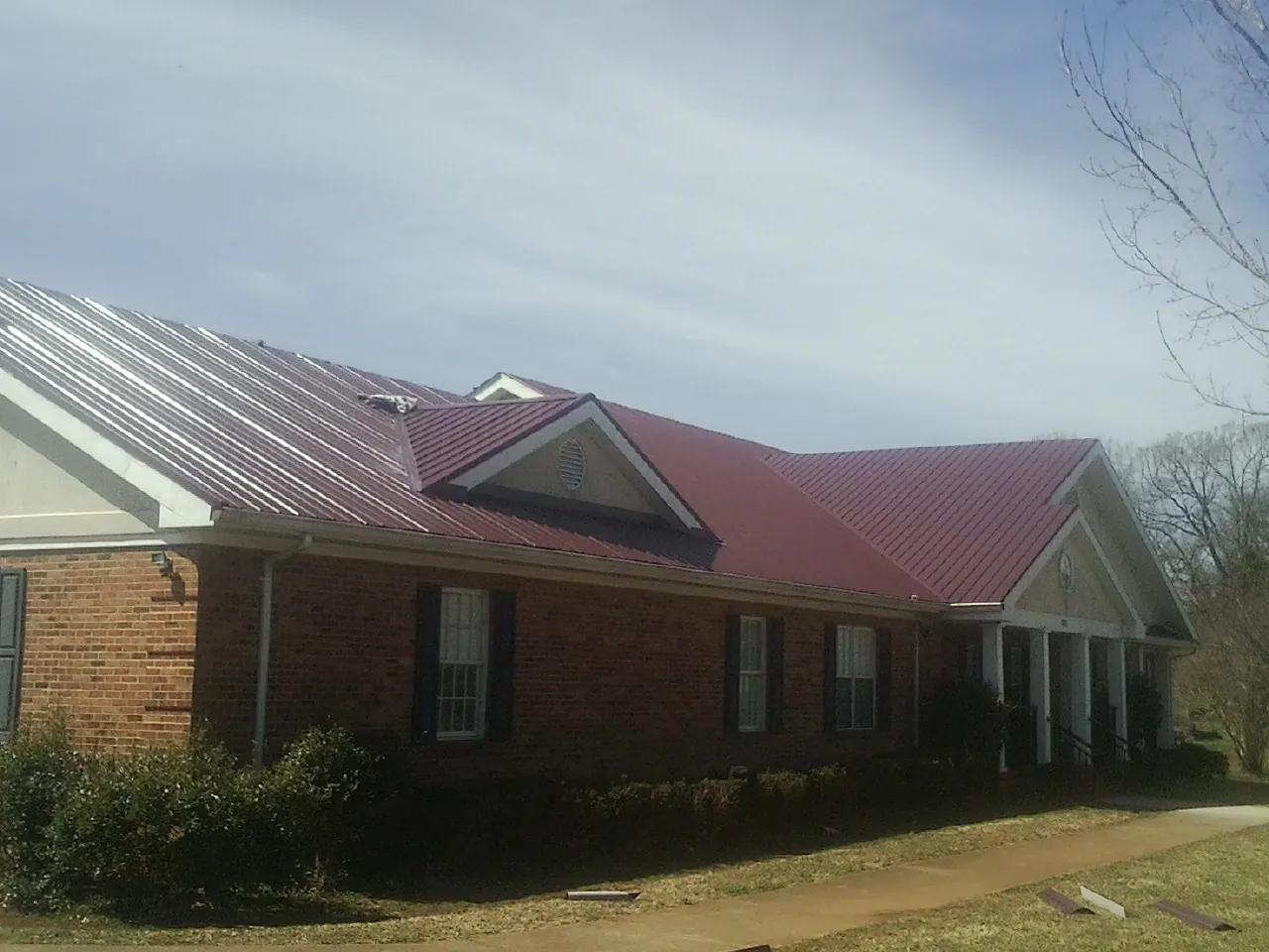 Red metal roof with gabled entries on a long brick building, from a Hail Damage Roof Repair job in Plainview