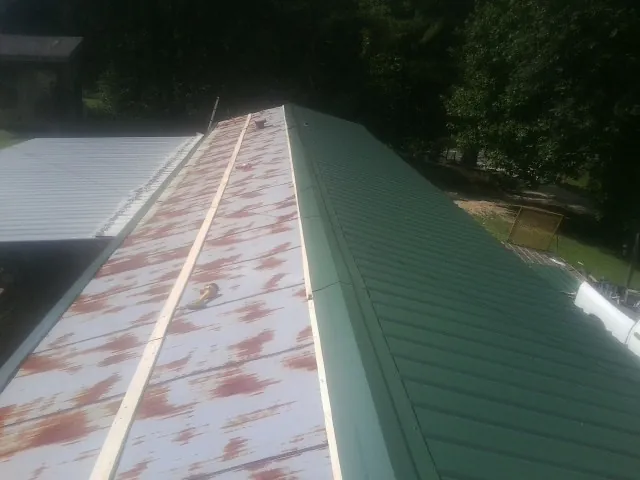 Old rusted panels beside newly installed green metal roofing — Wind Damage Roof Repair by Roofing Brothers in Plainview